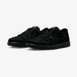 Travis Scott Jordan 1 Low Black Phantom sneakers shown in a front three-quarter view, featuring premium black suede, reverse Swoosh, white contrast stitching, and an all-black sole.